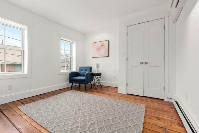 living area featuring a baseboard heating unit, baseboards, and hardwood / wood-style flooring