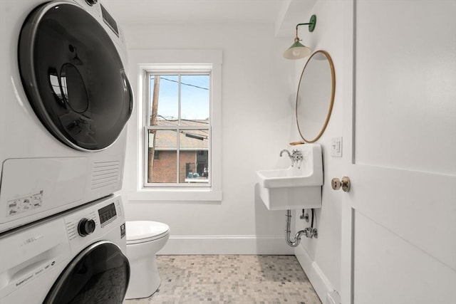 half bath featuring toilet, tile patterned floors, stacked washer and clothes dryer, and baseboards