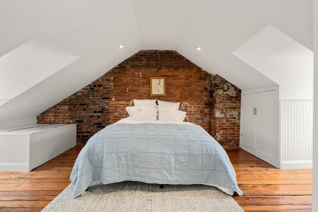 bedroom featuring vaulted ceiling, brick wall, and wood-type flooring