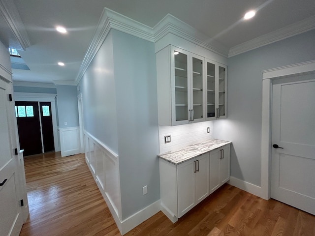 bar featuring hardwood / wood-style flooring, ornamental molding, white cabinets, light stone counters, and tasteful backsplash