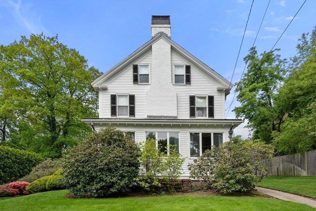 rear view of house featuring a lawn, a chimney, and fence