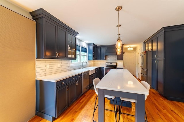 kitchen with appliances with stainless steel finishes, light wood-type flooring, backsplash, a sink, and a kitchen island