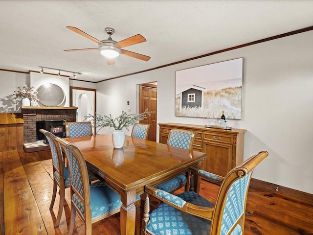 dining area featuring ceiling fan, ornamental molding, a fireplace, and hardwood / wood-style flooring