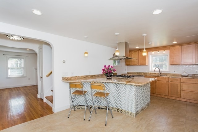 kitchen with decorative light fixtures, light hardwood / wood-style flooring, island range hood, sink, and light stone counters