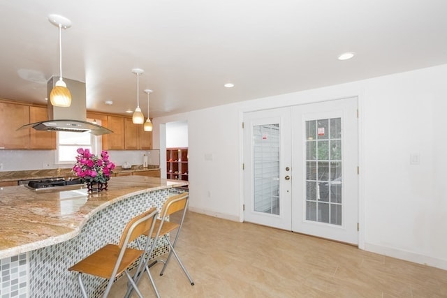 kitchen featuring hanging light fixtures, french doors, light stone counters, stainless steel gas cooktop, and a kitchen bar