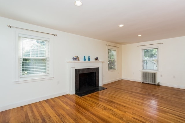 unfurnished living room featuring radiator heating unit, hardwood / wood-style flooring, a wealth of natural light, and a brick fireplace