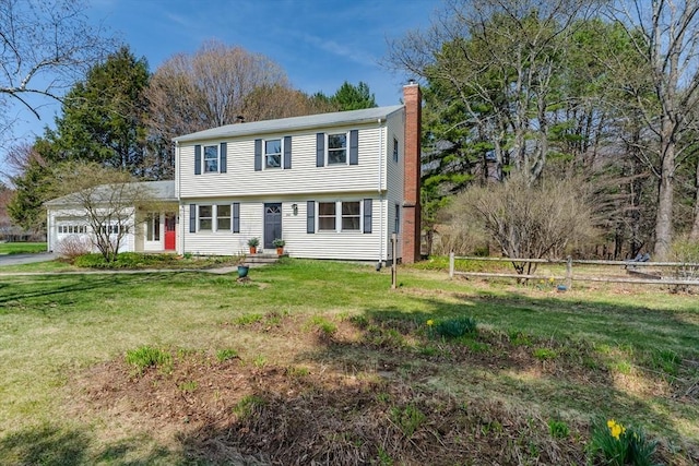 colonial house with a front yard, an attached garage, a chimney, and driveway