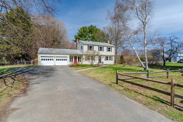 colonial-style house featuring a chimney, fence, a front lawn, an attached garage, and driveway