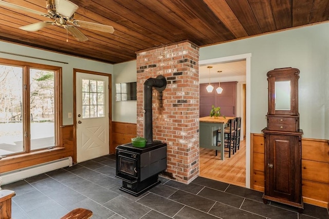 entryway with a wood stove, wooden ceiling, dark tile patterned floors, and wainscoting