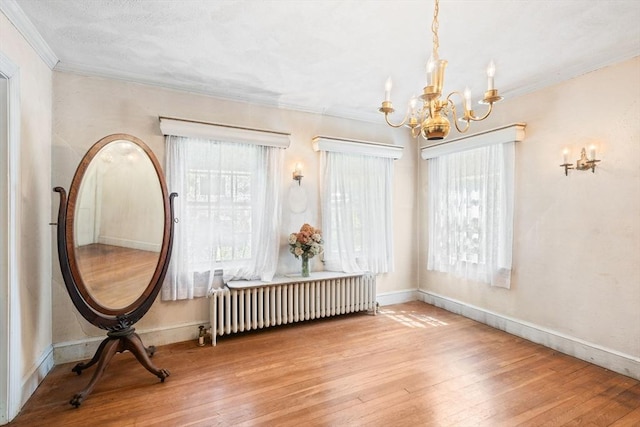 dining space with radiator heating unit, a chandelier, hardwood / wood-style floors, ornamental molding, and healthy amount of natural light