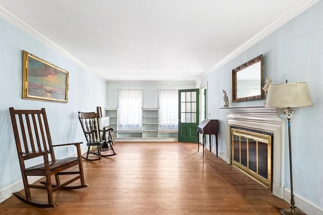 living area featuring wood finished floors, ornamental molding, and a glass covered fireplace