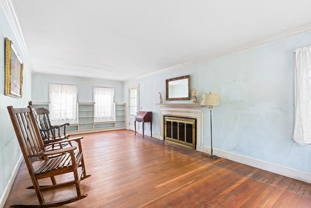 living area with crown molding, wood finished floors, baseboards, and a fireplace with flush hearth