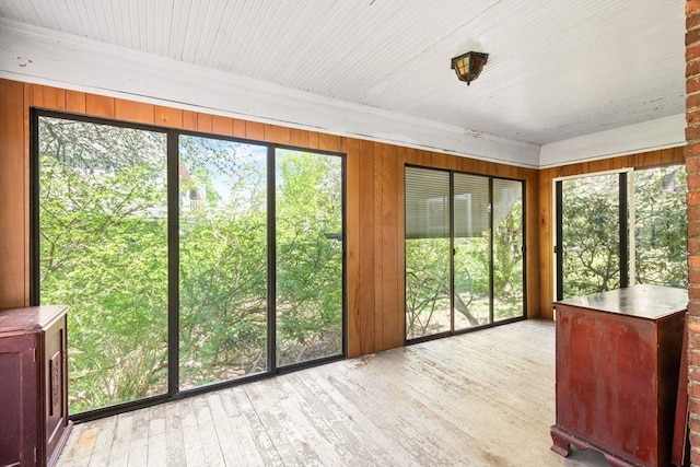 unfurnished sunroom featuring plenty of natural light, hardwood / wood-style floors, crown molding, and wood walls