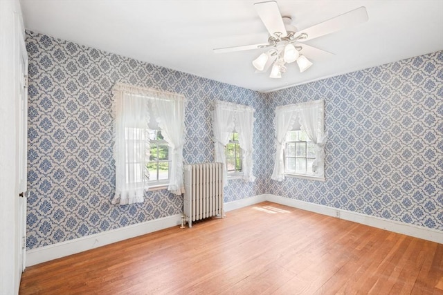 spare room with radiator heating unit, hardwood / wood-style flooring, wallpapered walls, baseboards, and a ceiling fan