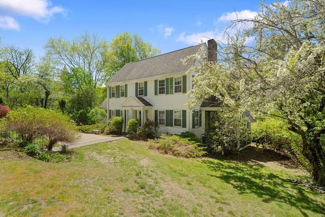 colonial-style house featuring a chimney, a front yard, and driveway