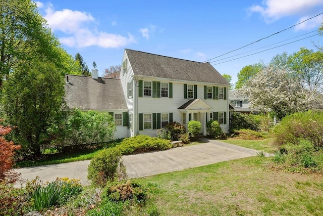 colonial inspired home with a front lawn and a shingled roof