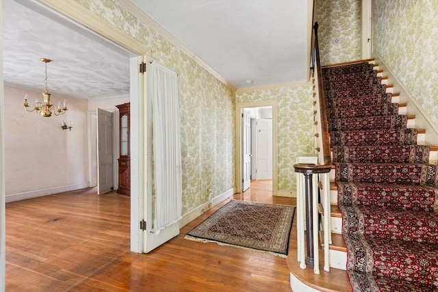 stairs featuring wallpapered walls, a chandelier, hardwood / wood-style floors, baseboards, and crown molding