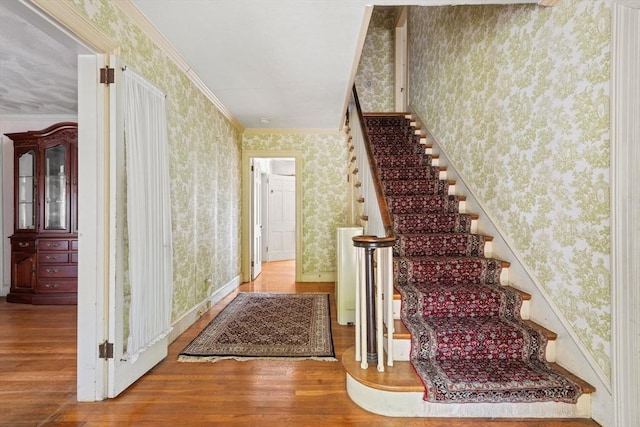 staircase featuring wallpapered walls, hardwood / wood-style floors, ornamental molding, and baseboards