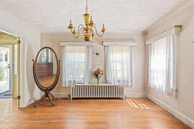 dining space with radiator, hardwood / wood-style flooring, a chandelier, plenty of natural light, and ornamental molding