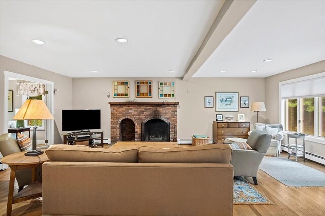 living room with light hardwood / wood-style flooring, a baseboard radiator, beamed ceiling, and a brick fireplace