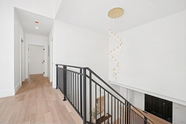 corridor with baseboards, recessed lighting, light wood finished floors, and an upstairs landing