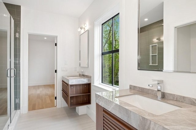 bathroom featuring wood finished floors, a sink, two vanities, and a shower stall