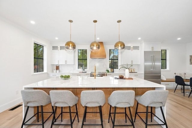 kitchen featuring stainless steel built in fridge, ornamental molding, a large island with sink, and white cabinetry