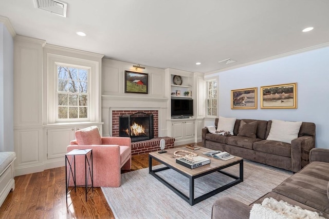 living room featuring visible vents, ornamental molding, built in features, wood finished floors, and a fireplace