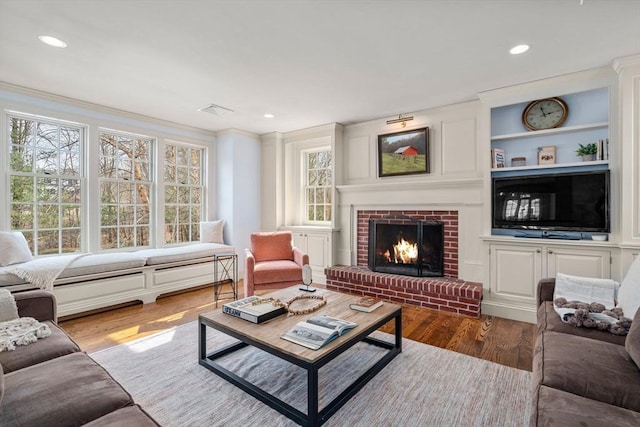 living room with visible vents, built in features, wood finished floors, a fireplace, and crown molding