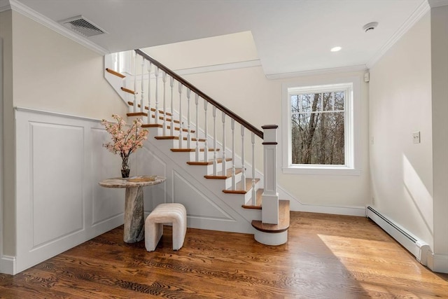 stairway with visible vents, baseboard heating, wood finished floors, and crown molding