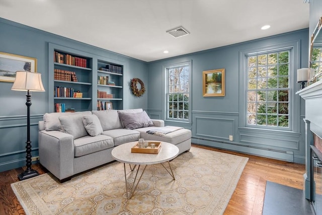 living area featuring a baseboard heating unit, a decorative wall, a fireplace with flush hearth, and built in shelves