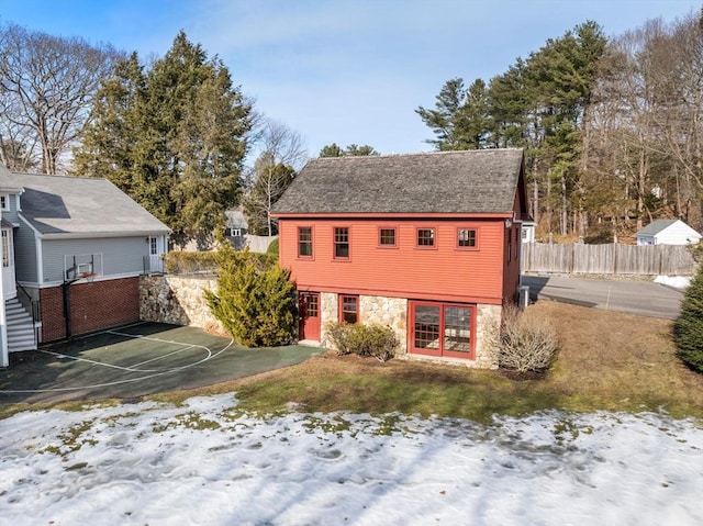 exterior space featuring basketball court, stone siding, and fence