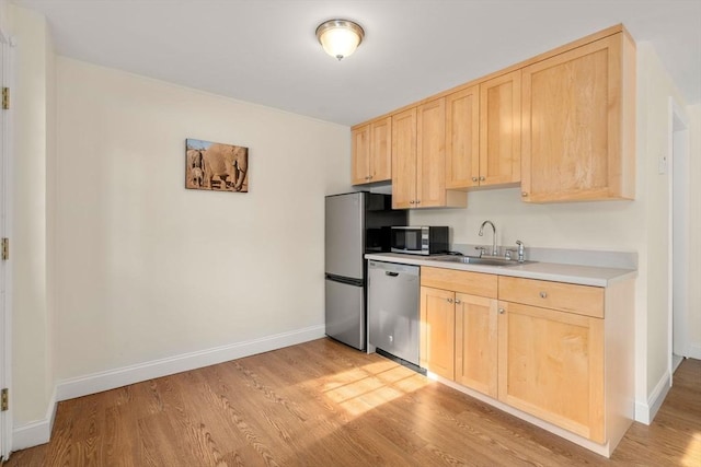 kitchen with light brown cabinets, light countertops, light wood-style flooring, stainless steel appliances, and a sink