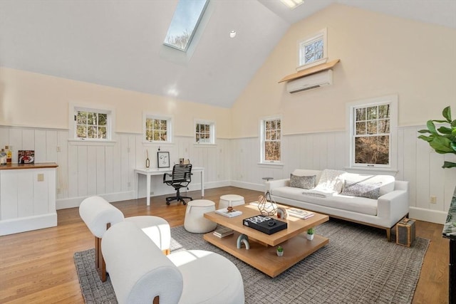 living area with a wainscoted wall, an AC wall unit, a wealth of natural light, a skylight, and light wood-style floors