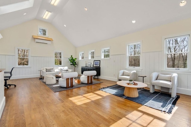 living room featuring high vaulted ceiling, wainscoting, a skylight, and wood finished floors