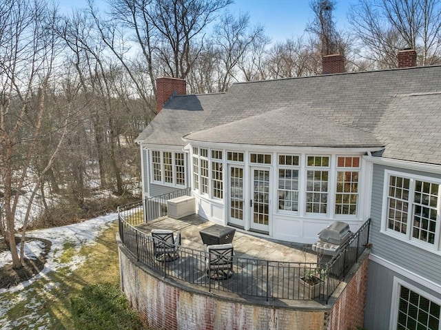 back of house featuring a chimney, roof with shingles, and a sunroom