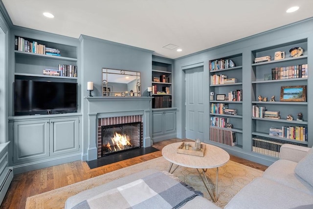 living area featuring built in shelves, wood finished floors, recessed lighting, a baseboard heating unit, and a brick fireplace