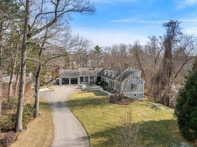 shingle-style home featuring aphalt driveway, an attached garage, a front yard, and a chimney