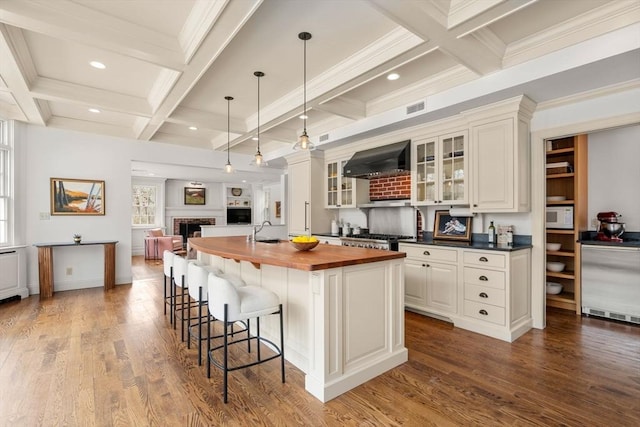 kitchen with a center island with sink, a sink, wood counters, ventilation hood, and white microwave