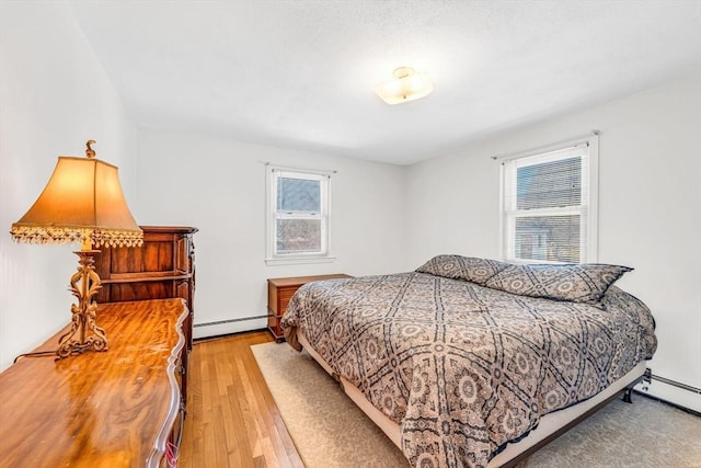 bedroom with light wood finished floors, multiple windows, and a baseboard heating unit