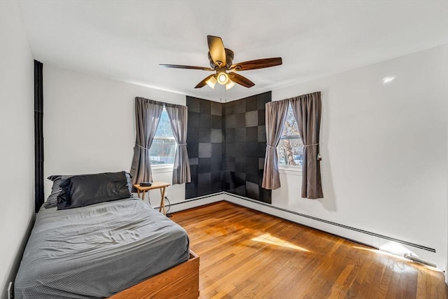 bedroom featuring a baseboard heating unit, multiple windows, hardwood / wood-style flooring, and a ceiling fan