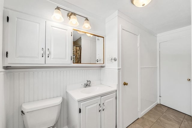 bathroom featuring a wainscoted wall, crown molding, vanity, and toilet