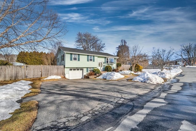 raised ranch with driveway, an attached garage, and fence