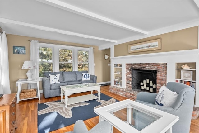 living room featuring a brick fireplace, built in features, beam ceiling, and wood finished floors