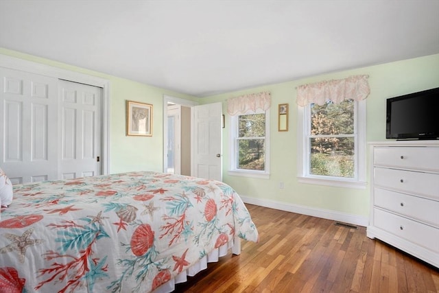 bedroom featuring a closet, wood-type flooring, visible vents, and baseboards