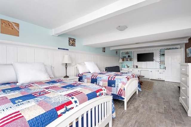 bedroom with a wainscoted wall, beamed ceiling, and wood finished floors