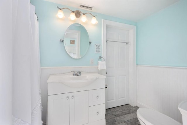 bathroom with a wainscoted wall, curtained shower, visible vents, toilet, and vanity