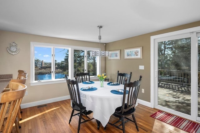 dining space featuring baseboards, a water view, visible vents, and hardwood / wood-style floors