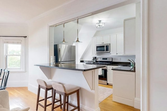 15 Garrison Rd, Brookline, MA 02445 - kitchen featuring appliances with stainless steel finishes, dark countertops, light wood-style flooring, a kitchen breakfast bar, and ornamental molding