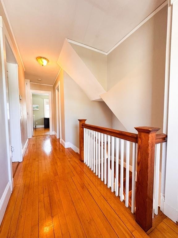corridor with an upstairs landing, ornamental molding, light wood-style flooring, and baseboards